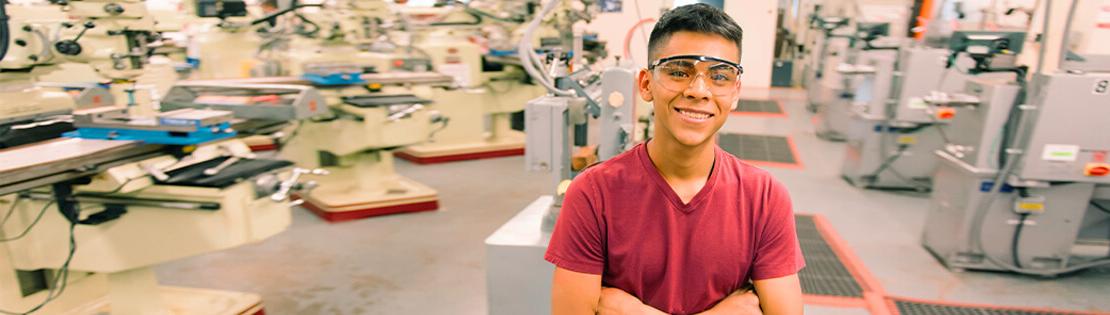 一个学生戴着安全眼镜在仓库里微笑
